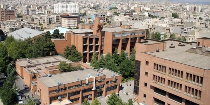 Aerial view of a university campus with brown brick buildings, courtyards and trees, city skyline in the distance.