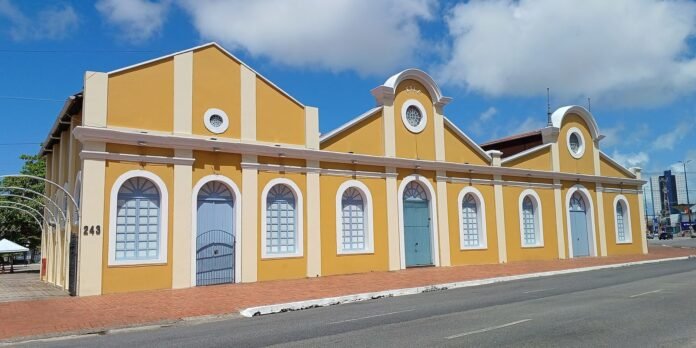 Yellow historic building with white trim and a row of arched blue doors along a brick sidewalk under a blue sky.