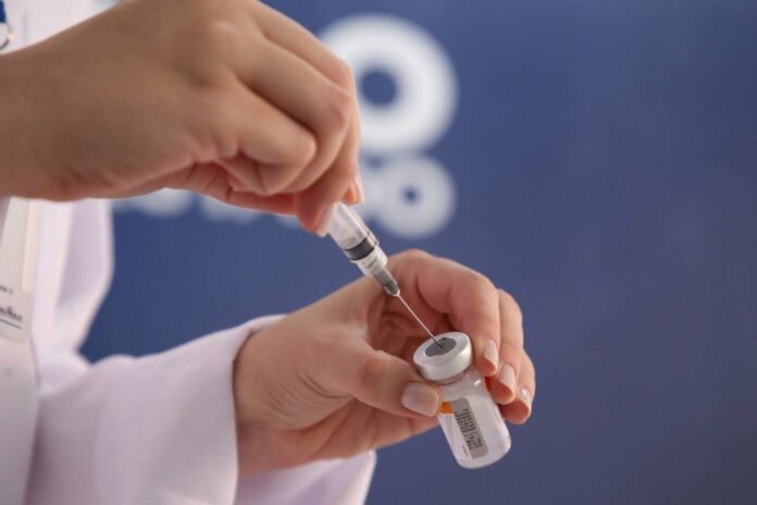 Healthcare worker drawing liquid from a vial into a syringe for vaccination.