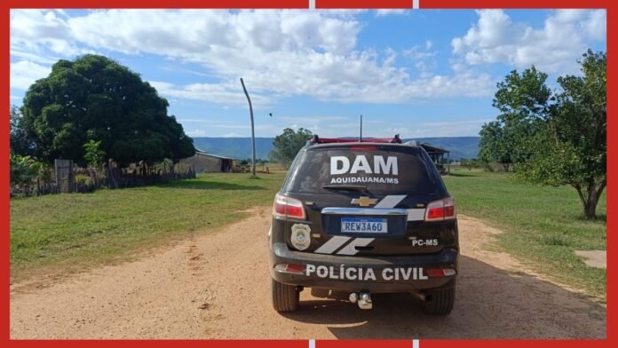 Back view of a black Polícia Civil SUV with DAM Aquidauan/MS markings parked on a dirt road in a rural landscape under a blue sky with clouds.
