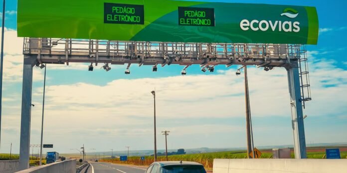 Electronic toll collection banner spans a highway, with green Ecovias sign and text 'Pedágio Eletrônico' overhead the road