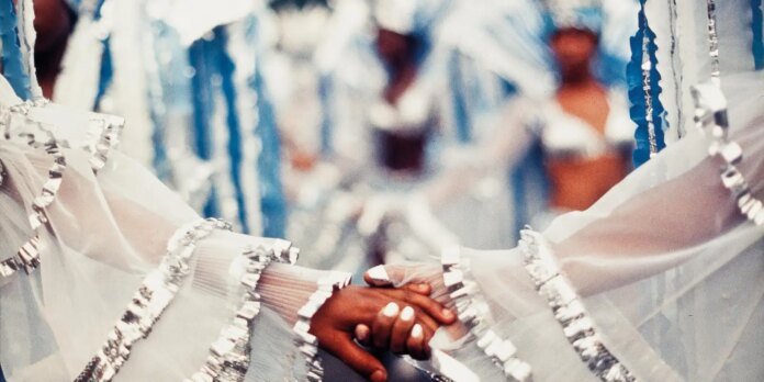 Two dancers in white outfits with silver trim clasp hands in a circle.