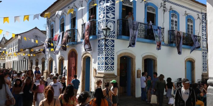 Crowded street festival in front of a decorative blue-and-white tiled building with hanging banners and portraits on the balconies.