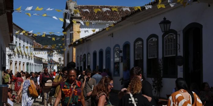 Crowded sunny street lined with white buildings, blue arched windows, and yellow-white pennant flags overhead.