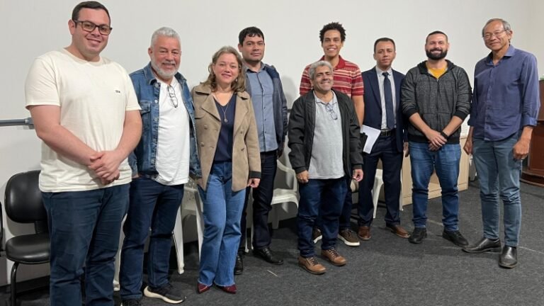 Group of ten adults posing together in a casual meeting room, smiling at the camera.