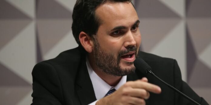 Man in a dark suit speaks into a handheld microphone during a panel discussion.