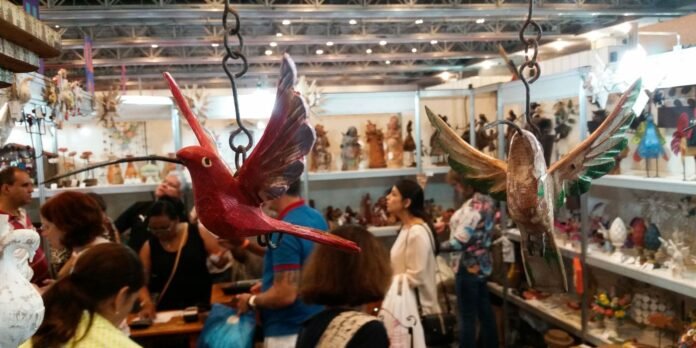 Two wooden hummingbird sculptures hanging from chains in a busy craft market stall.