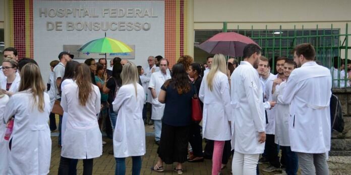 Group of doctors and nurses in white lab coats standing outside a hospital entrance with colorful umbrellas in the background.