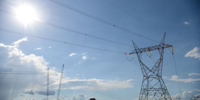 Sunlit blue sky with a tall metal transmission tower on the right and power lines crossing the scene.