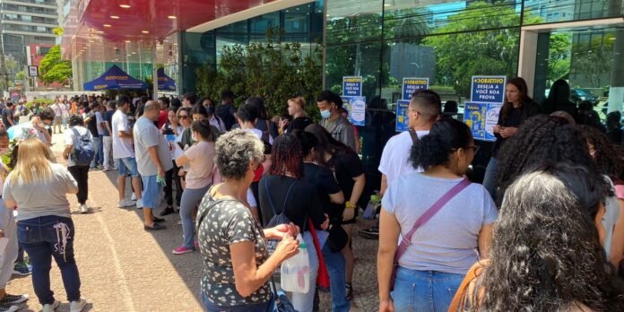 A crowd of people lined up outside a modern glass building for an event or service.