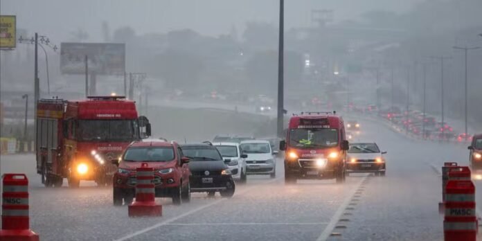 Emergency vehicles and cars on a wet highway under heavy rain, with orange traffic barrels and headlights shining through the spray