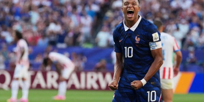 Soccer player in blue France kit with number 10 celebrates on the pitch, fists clenched and mouth open in celebration.