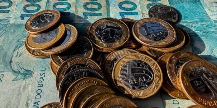 Close-up of stacked and scattered Brazilian reais coins on top of blue 100 reais banknotes.