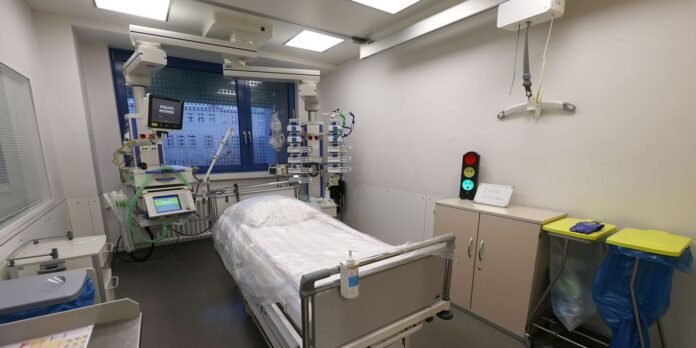Hospital ICU bed with multiple life-support machines, monitors, and tubing in a bright clinical room with a window behind.