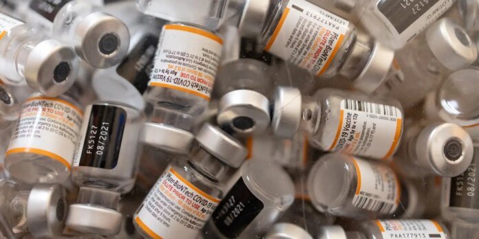 Pile of Pfizer-BioNTech COVID-19 vaccine vials with orange labels and metal caps