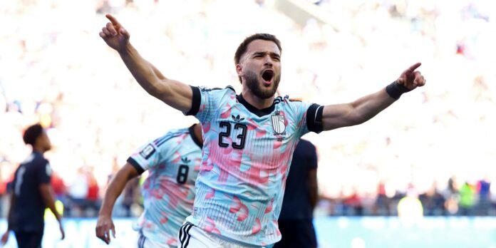 Male soccer player in a light blue-pink jersey (#23) celebrates with arms raised and mouth open.