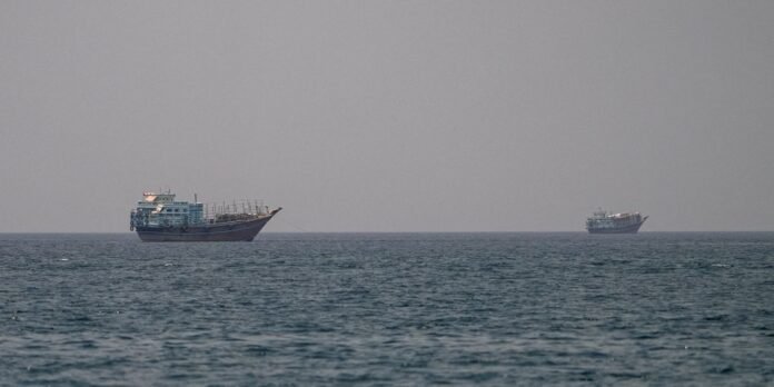 Two fishing boats on calm sea, one larger on the left and a smaller one farther away on the right under a clear gray sky.