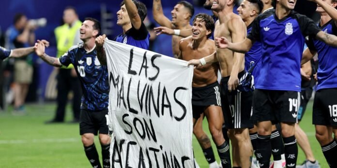 Argentinian soccer players celebrate on the field, holding a white banner that reads 'LAS MALVINAS SON ARGENTINAS'.] ,