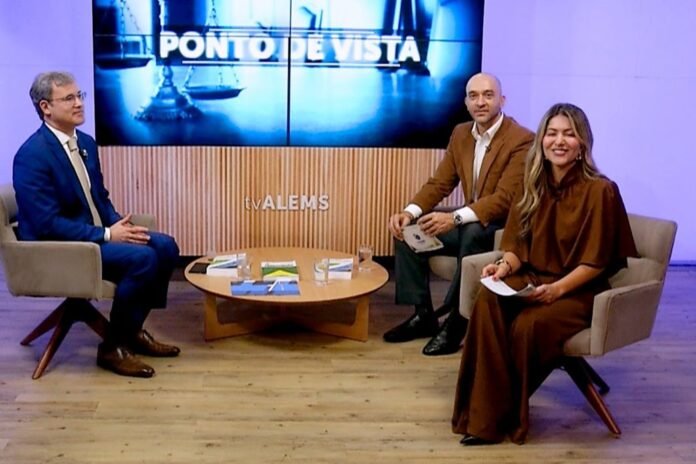 Three TV hosts seated around a round table in a studio; a large screen behind reads 'PONTO DE VISTA'.
