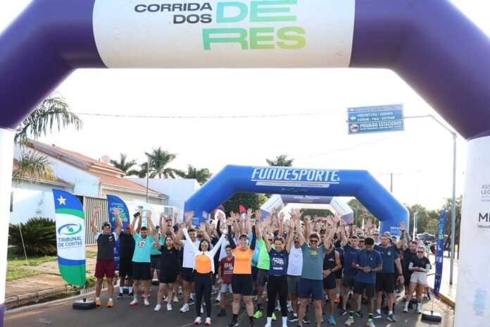 Group of runners at the start line of a race under a large inflatable arch, hands raised in celebration before the start.