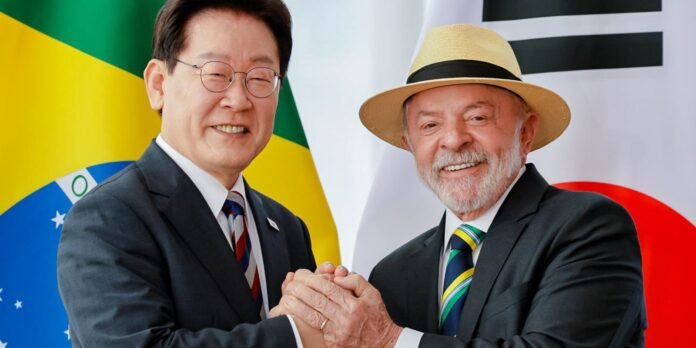 Two men in suits shake hands and smile, with the Brazil and Japan flags in the background.