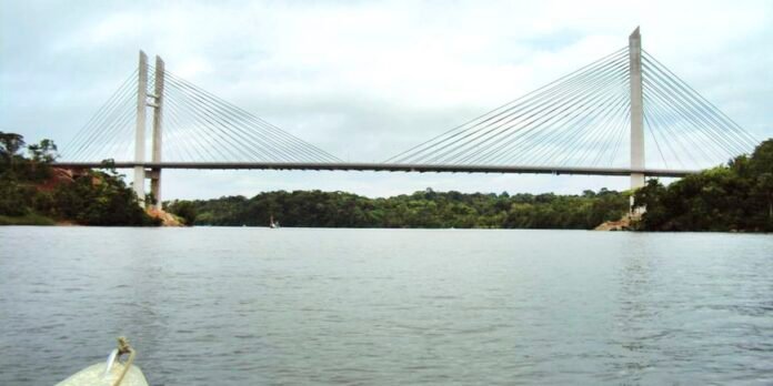 Cable-stayed bridge spanning a wide river with two tall pylons and numerous supporting cables, green shores on both sides.