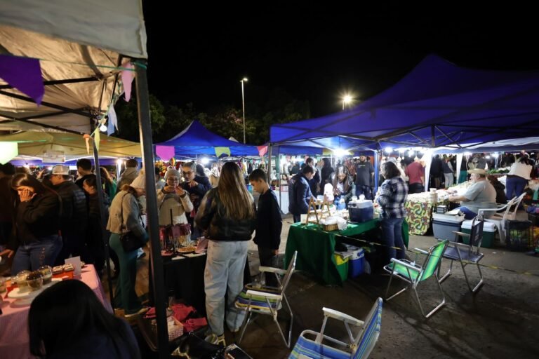 Night market scene with several stalls under colorful canopies and crowds browsing at dusk.