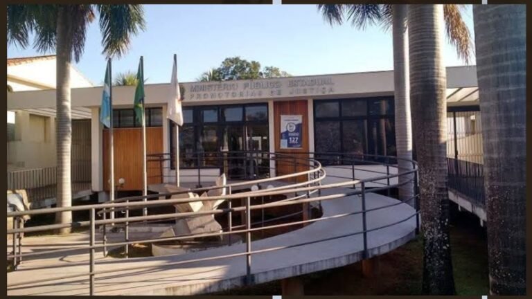 Entrance to a public building with a curved ramp, glass doors, and several flagpoles with flags in front of the entrance.