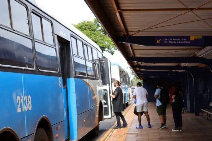 Blue city bus at a platform with doors open, people boarding and a covered station ahead.