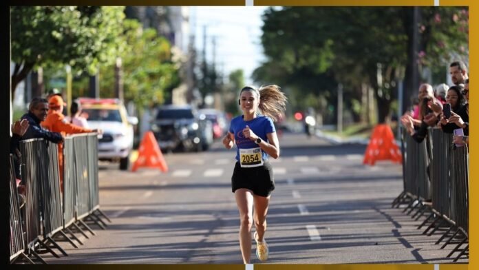 Female runner in a blue shirt and black shorts with bib 2054, mid-race on a city street lined with barriers and cheering spectators.