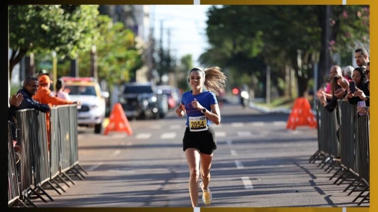 Female runner in a blue shirt and black shorts with bib 2054, mid-race on a city street lined with barriers and cheering spectators.