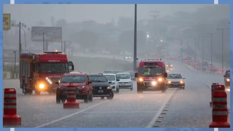 Flooded highway with vehicles driving through heavy rain; two red fire trucks and a red SUV in the foreground, orange traffic cones along the road.