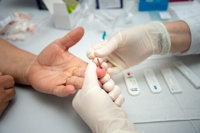 Gloved technician pricking a patient's finger with a lancet for a rapid blood test.