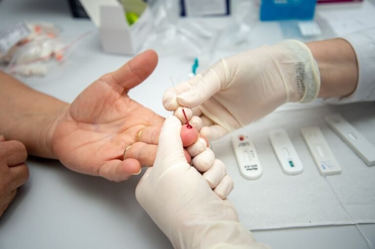 Gloved technician pricking a patient's finger with a lancet for a rapid blood test.