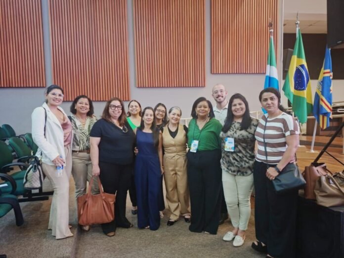 Group of diverse adults posing together in a conference room, smiling for a photo with green chairs and flags in the background.