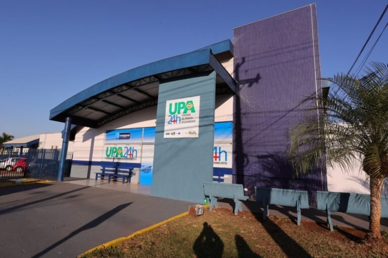 Front of a UPA 24h urgent care center with blue facade, curved roof, and blue benches outside.