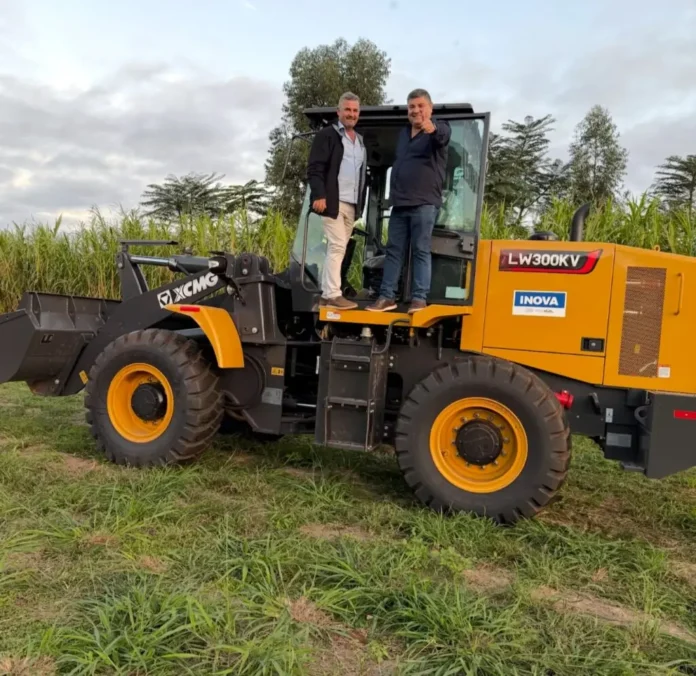 Two men standing on the steps of a large yellow XCMG loader in a grassy field, posing for the photo.