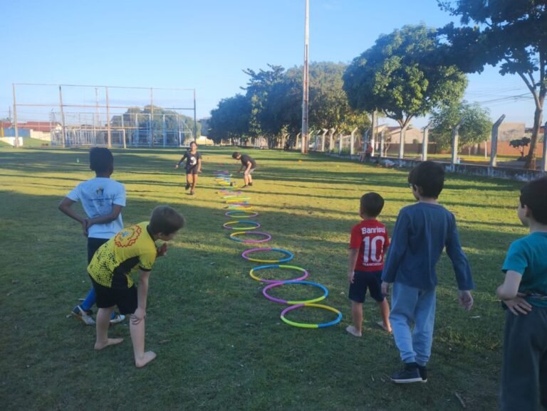 Group of children outdoors on a grassy field, preparing to run through a line of colorful hoops laid out as an obstacle course.