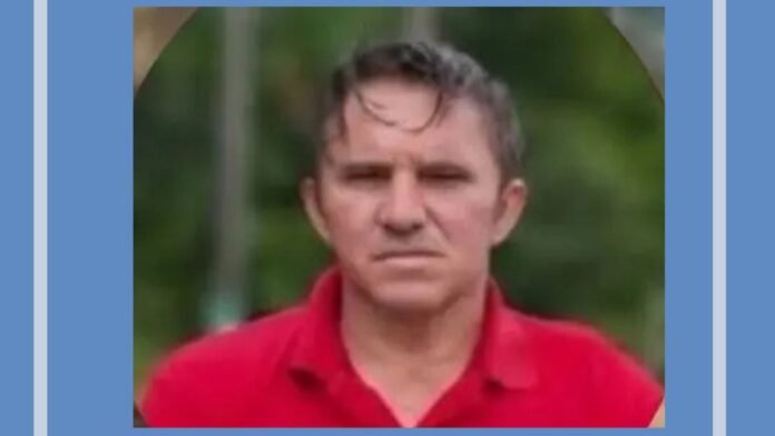 Middle-aged man with short hair in a red polo shirt, outdoors with greenery in the background on a blurred backdrop.