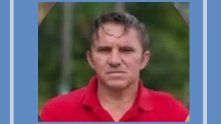 Middle-aged man with short hair in a red polo shirt, outdoors with greenery in the background on a blurred backdrop.