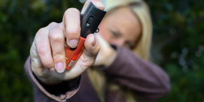 Person holding a red disposable lighter toward the camera outdoors.