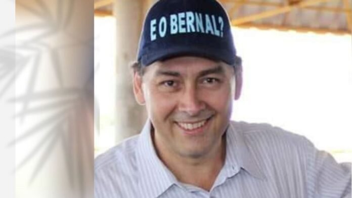Smiling man wearing a navy cap with teal text, outdoors.