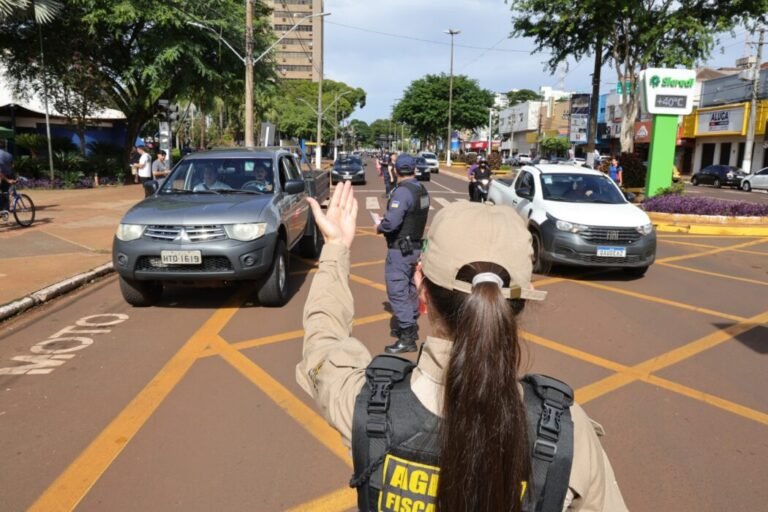 Traffic stop: female officer in uniform facing a road with cars, raising her hand to signal stops on a city street.