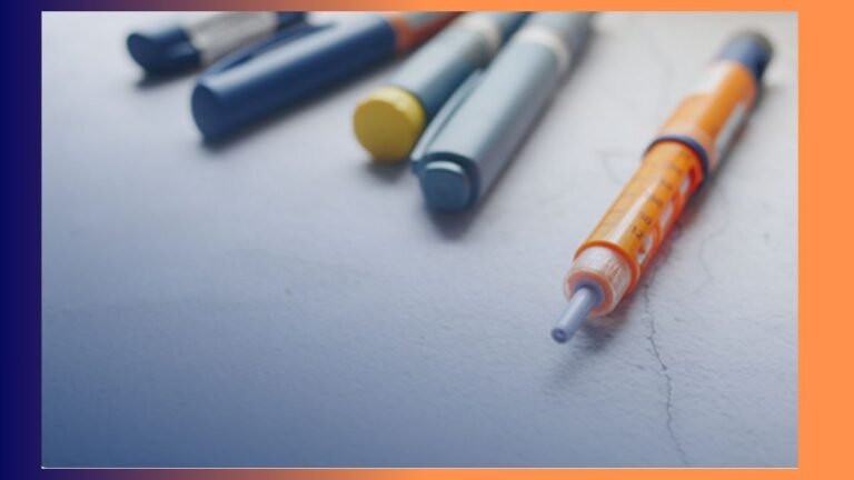 Close-up of a syringe with an orange plunger lying on a pale surface, with blurred colorful marker caps in the background.