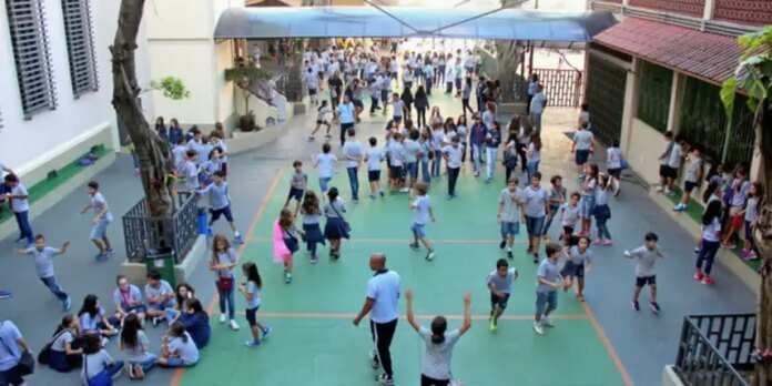 Crowd of students in blue uniforms socializing and playing in a school courtyard with a green play surface.