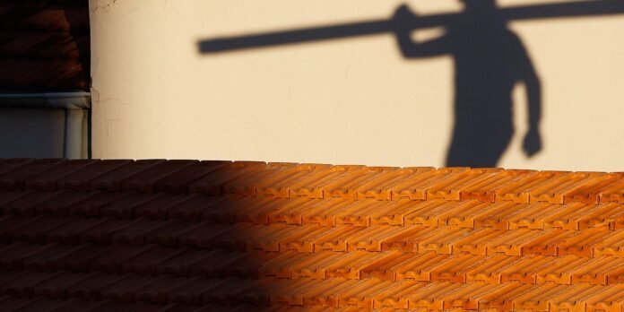 Terracotta roof tiles bathed in sunlight with the shadow of a person carrying a long object on a pale wall.