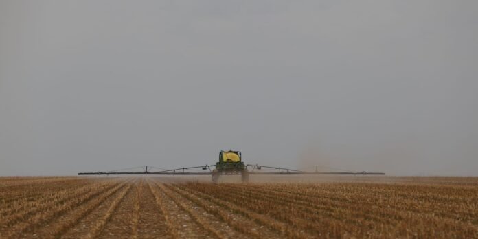 Center-pivot irrigation rig spraying water across a dry harvested field under a gray sky.