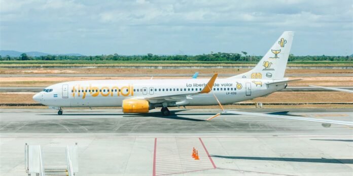 White passenger jet with yellow-orange accents taxiing on a runway at an airport, Flybondi livery visible on the fuselage and tail decals.