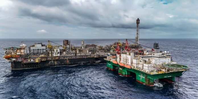 A large offshore oil rig connected to a green support vessel at sea under a cloudy sky.