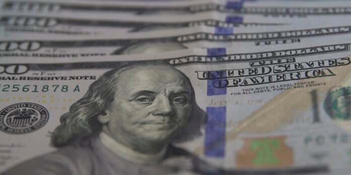 Close-up of stacked US $100 bills featuring Benjamin Franklin and blue security strips visible in the foreground